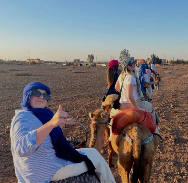 Traveler riding a camel in the Erg Chebbi desert with luxury camp tents in the background at sunset