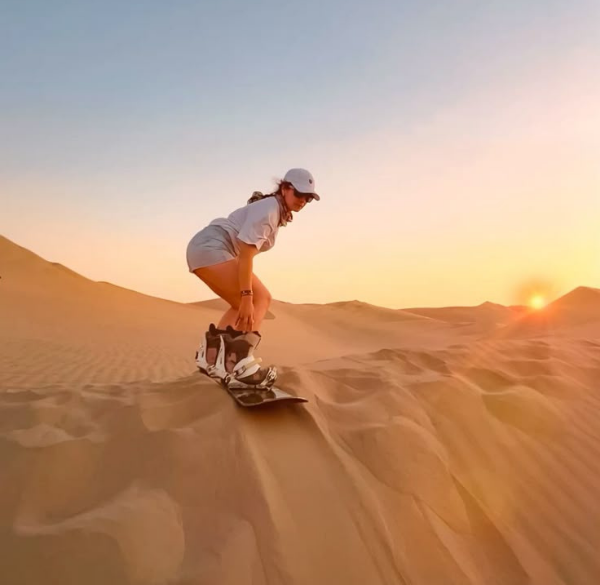 Traveler sandboarding down a tall golden dune at sunset in the Merzouga Sahara Desert, Morocco